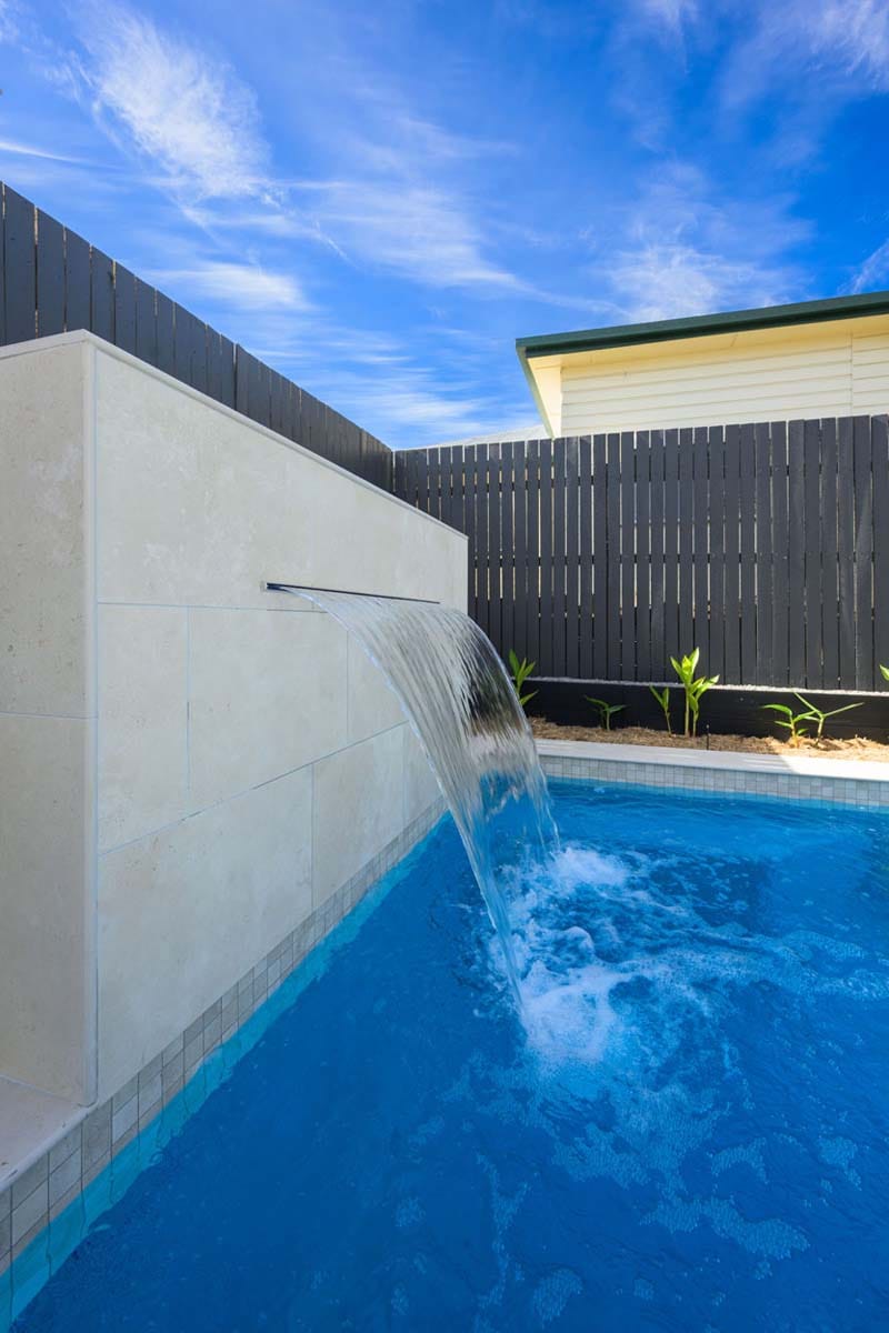 Flax Travertino - 20mm 5 Porcelain travertine-look tiles used around a calming pool water feature in a warm, minimalist setting.