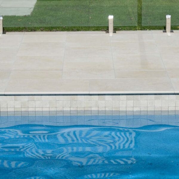 Travertine-look porcelain tile at pool waterline, creating a light Mediterranean feel.